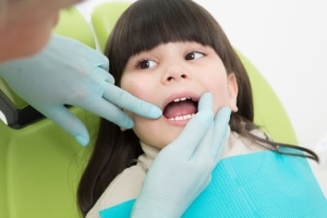 menina deitada sobre cadeira de dentista tendo dentes examinados
