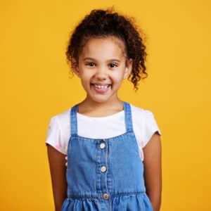 menina de seis anos morena sorrindo sobre fundo amarelo