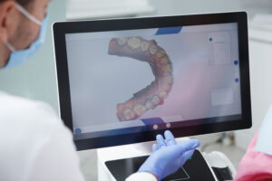 Profissional da odontologia analisando imagem digital 3D da arcada dentária em um monitor.